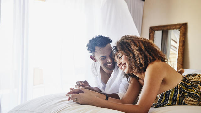 Medium wide shot of smiling couple relaxing on bed in luxury suite at tropical resort 