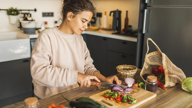 Woman cutting fresh organic vegetables for salad on kitchen. Sustainable lifestyle 