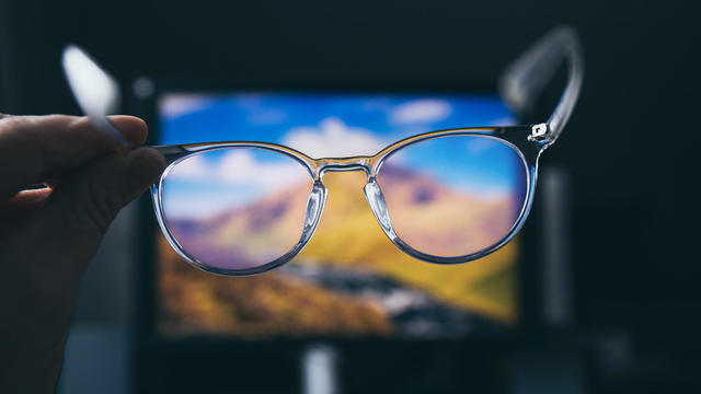 Selective focus on transparent clear blue light computer glasses and computer screen glowing on the background in home or office. Blue light glasses protect eyes and eyesight from screens blue light. 